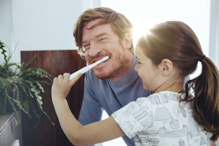 Daughter brushing her father?s teeth in bathroom